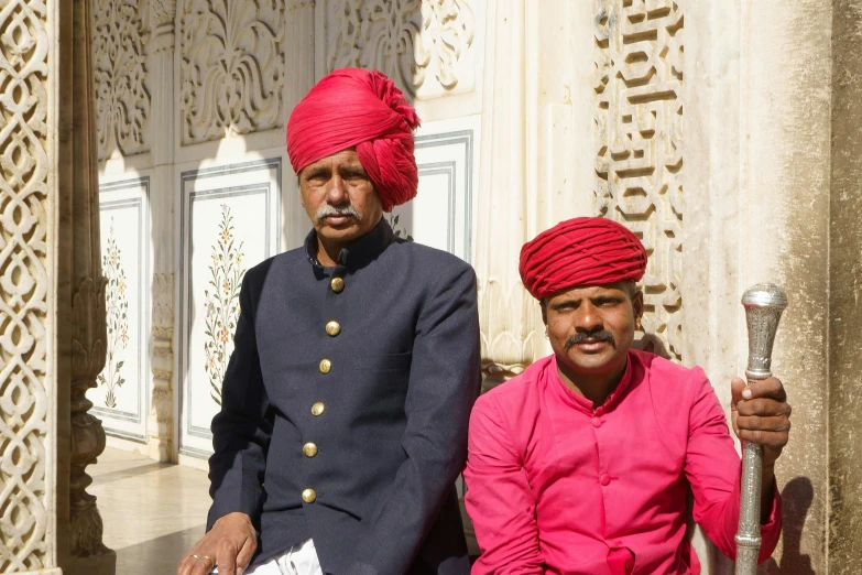two men wearing bright red turbans sitting outside of a building