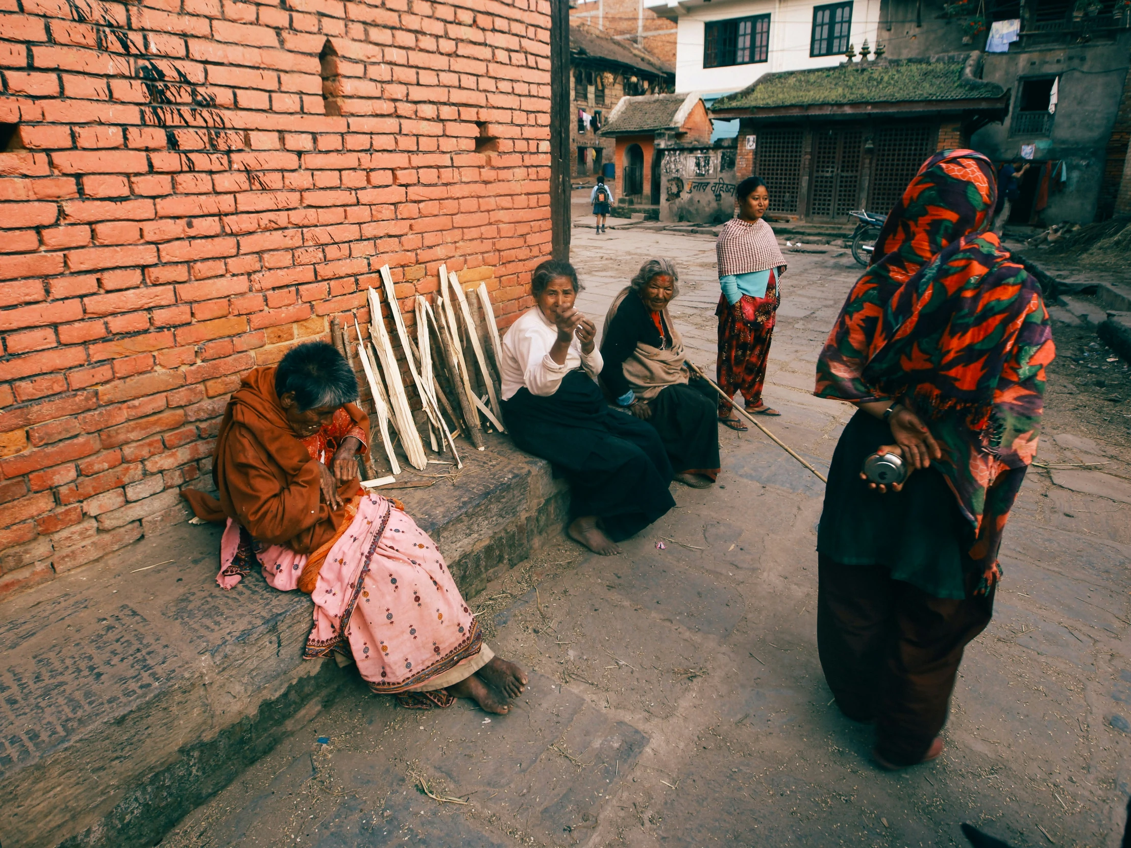 three indian women sitting against a brick wall while a man sits