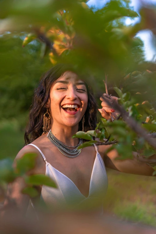 a woman smiles and holds up leaves from a tree