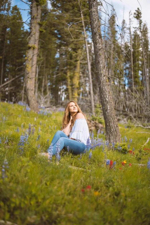 a beautiful young lady in blue jeans sitting in the middle of some flowers