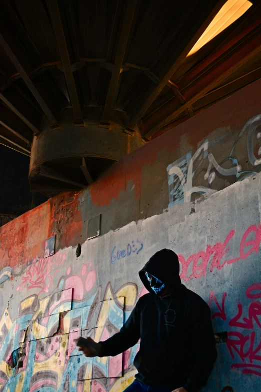 a man wearing a neon mask next to a wall covered in graffiti