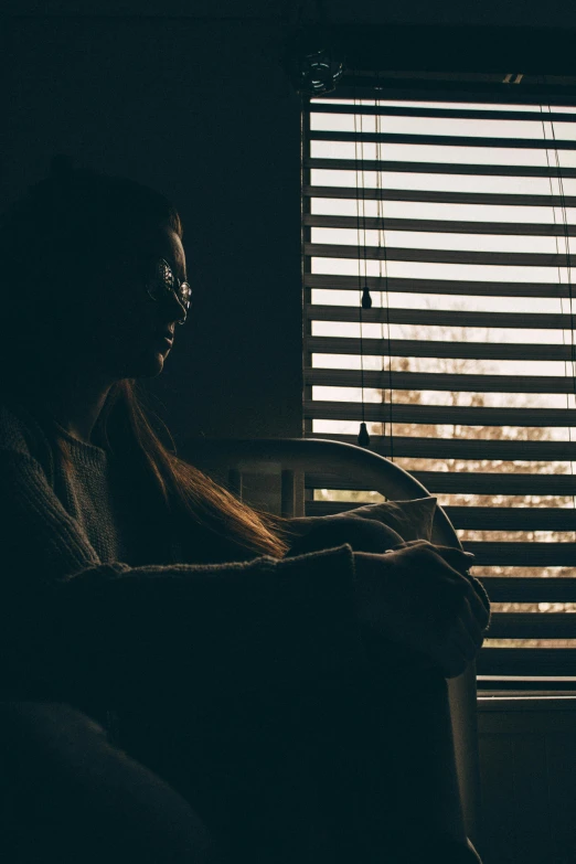 a woman sits in front of a window with blinds