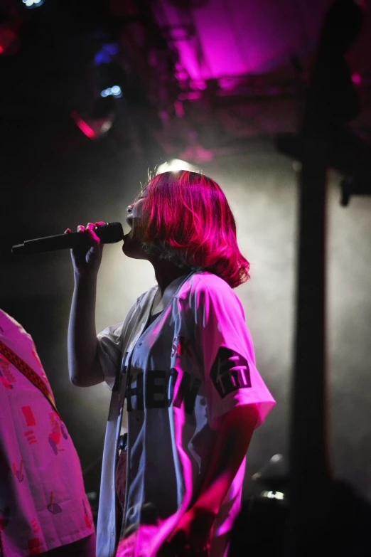 a person singing on stage with pink light coming from behind