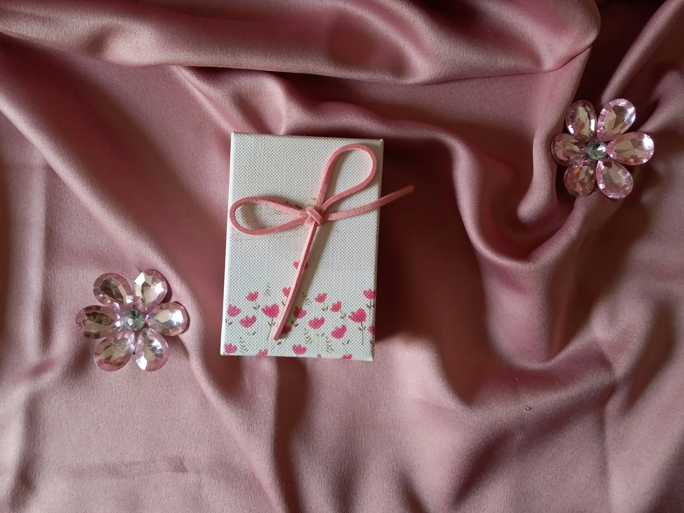 a wrapped gift and flower decorations sit on a pink satin fabric