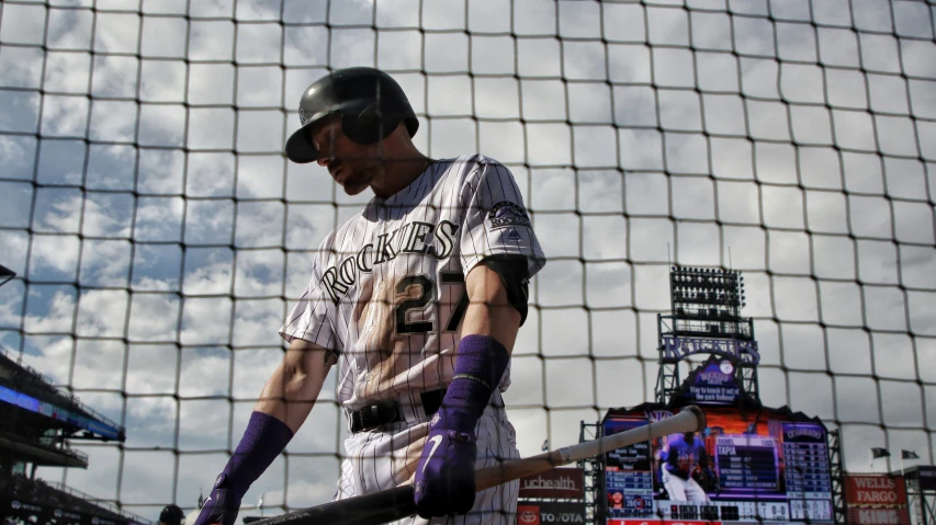 a baseball player walks next to his bat in the batting cage