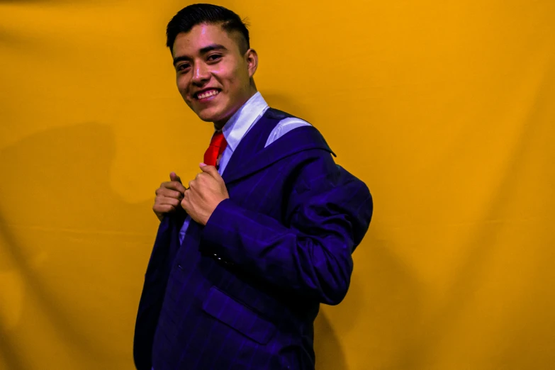 a man standing against a yellow backdrop wearing a purple jacket and red tie