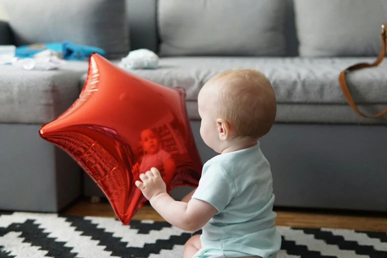 a baby holding up a red balloon next to a couch