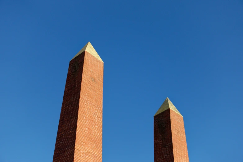 two tall brick obelisks near each other against a blue sky