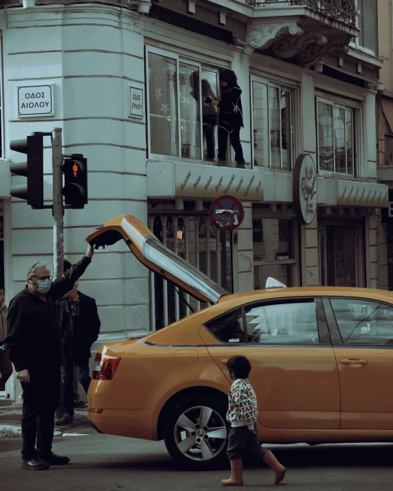 a yellow car is pulling down the street as people stand on top of it