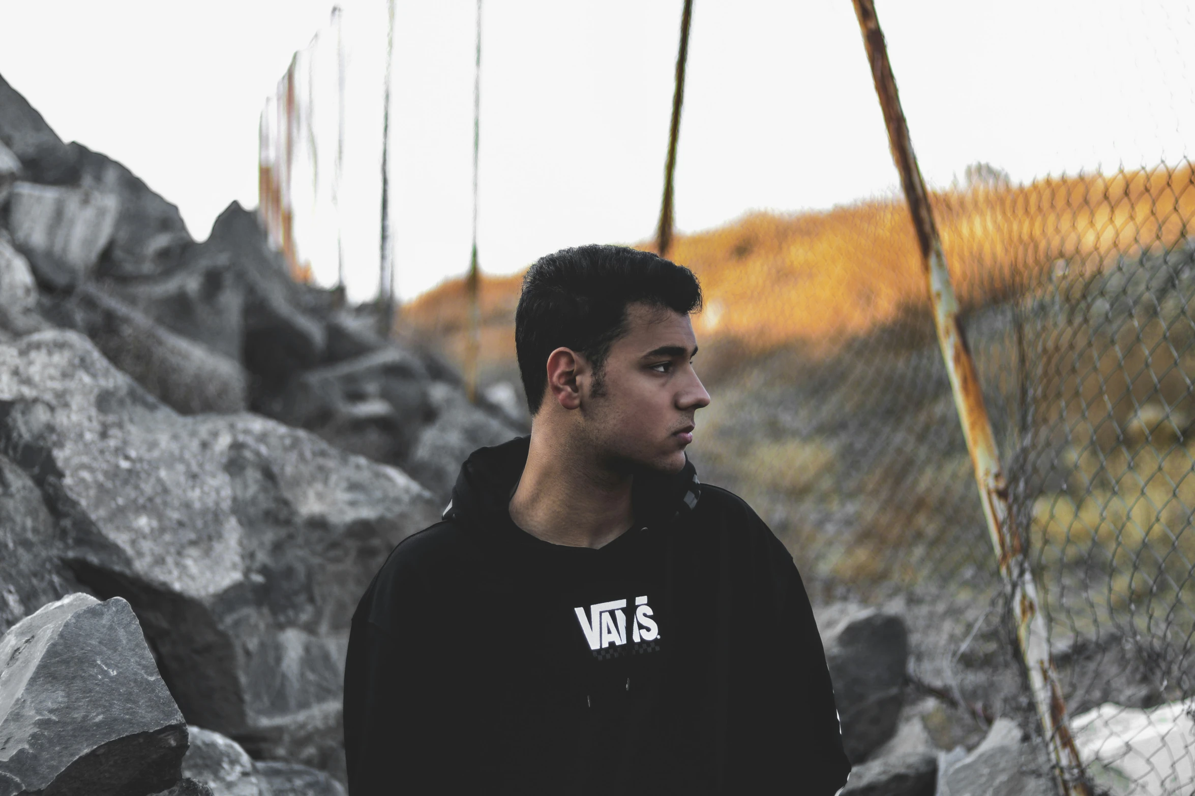 a young man standing by a fence with a cell phone