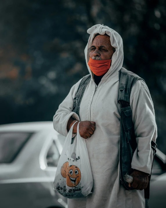 an elderly man wearing a face mask in front of a car