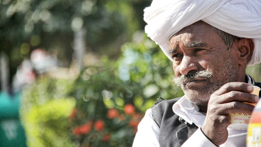 an old man in a turban holding a bottle of alcohol