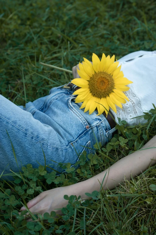 a young woman lays on the ground, under a sunflower