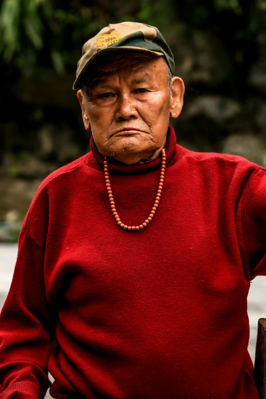 an elderly man in a red sweater looks off into the distance