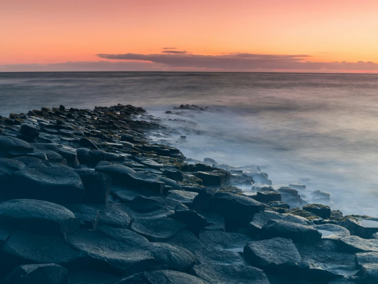 a surfboard laying on the rocks by the ocean at sunset