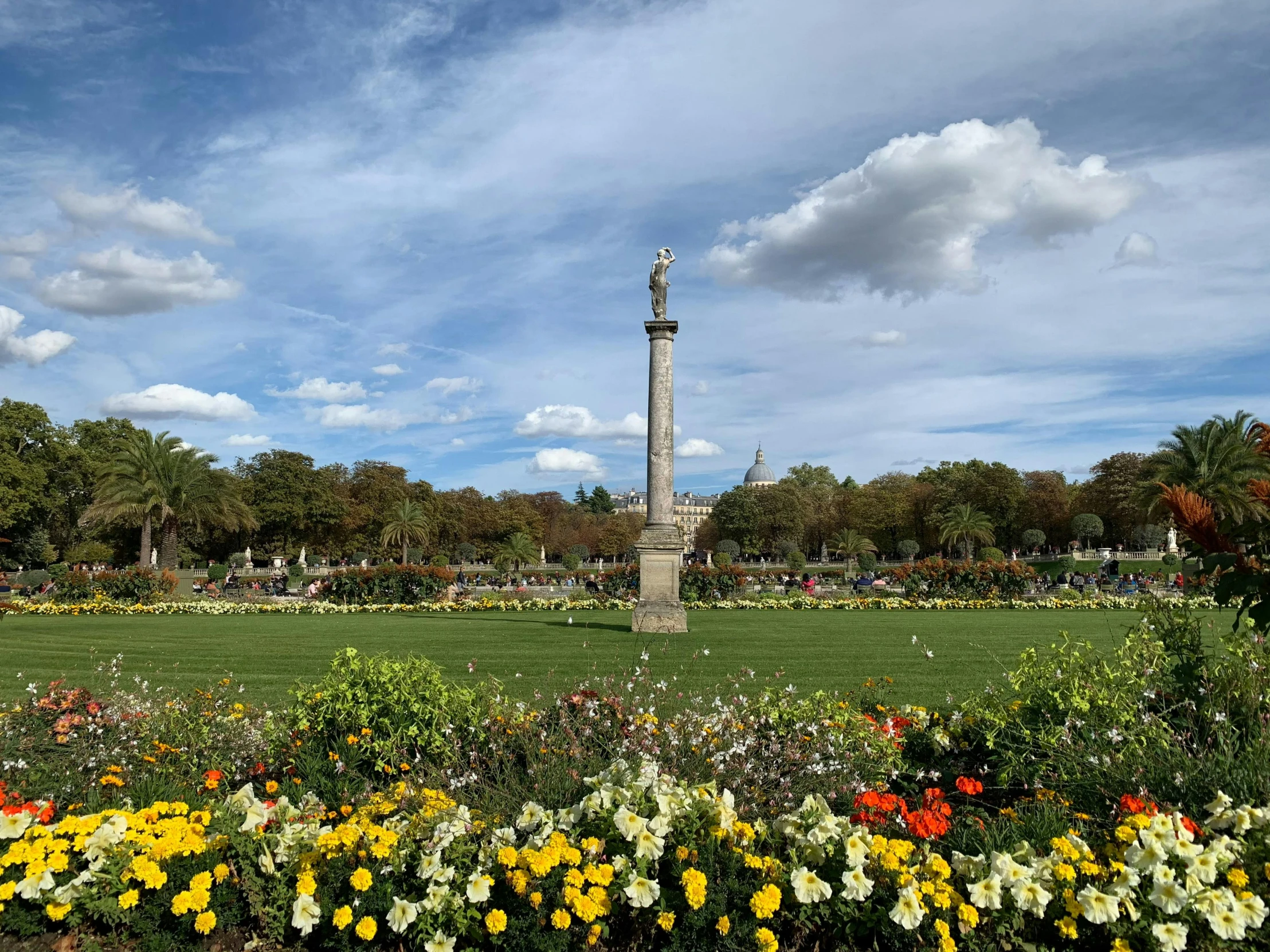 a flowered flower garden in the middle of a park with a tall statue