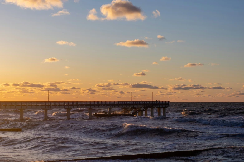 pier in the ocean at sunset with some clouds