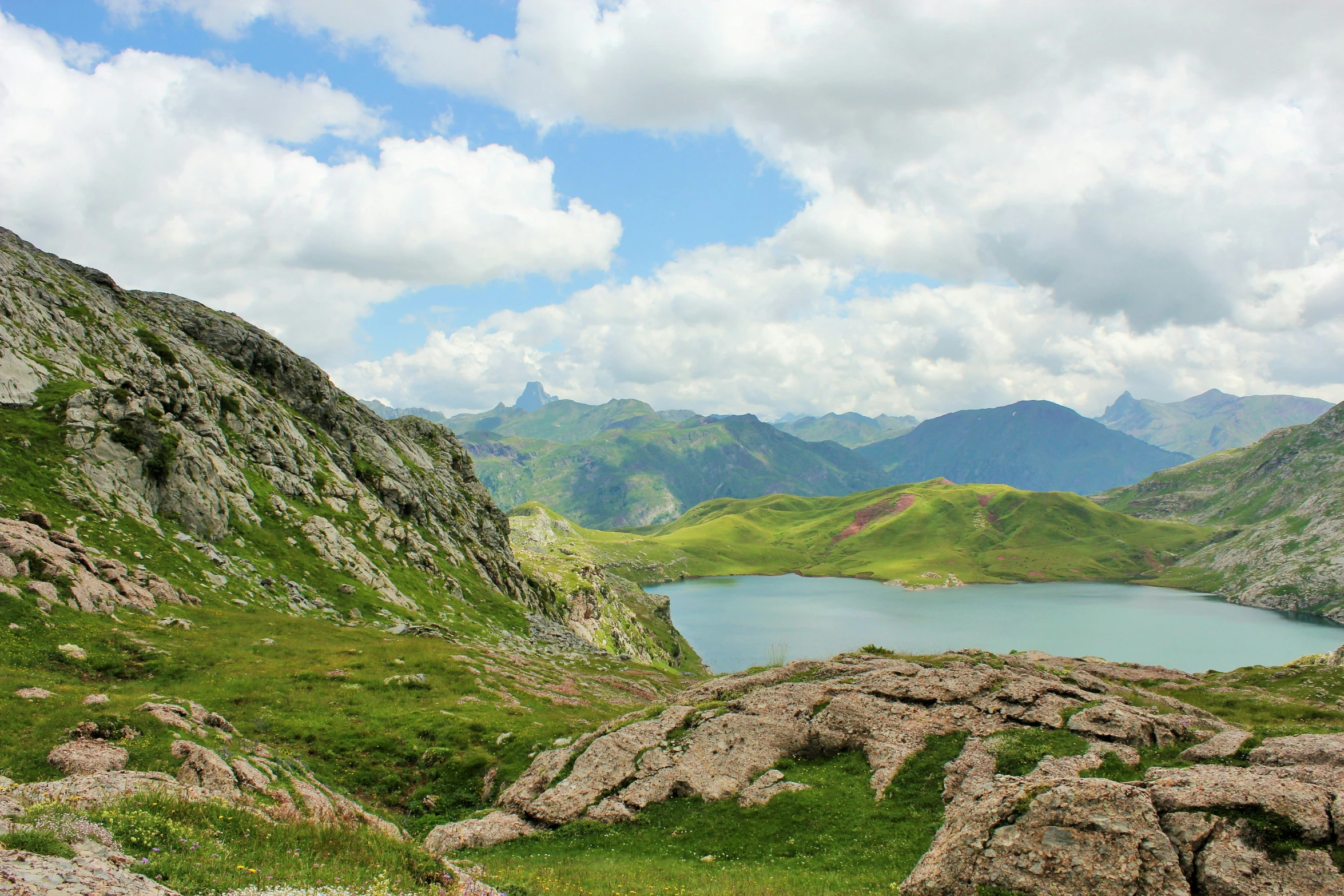 an area of rocky land with blue water, grass and mountains