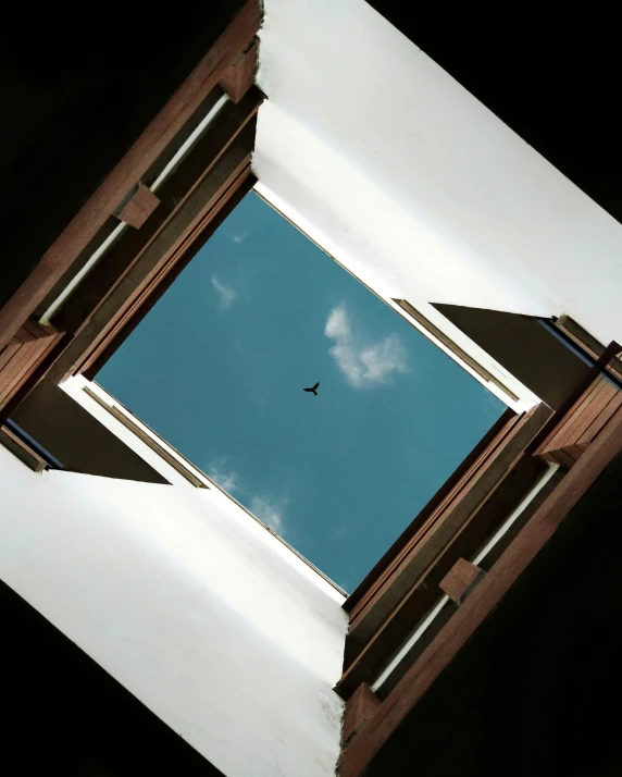 a view from a window shows the top of a building with a bird flying in the sky