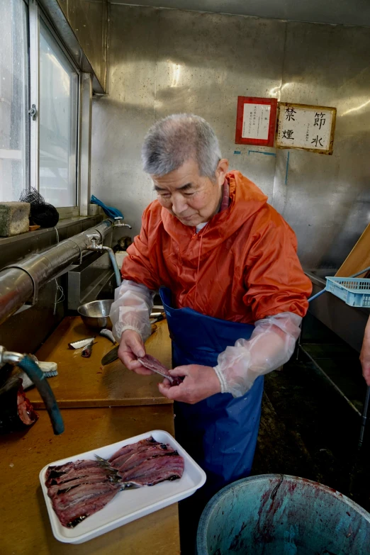 an older man in an orange jacket is preparing steak