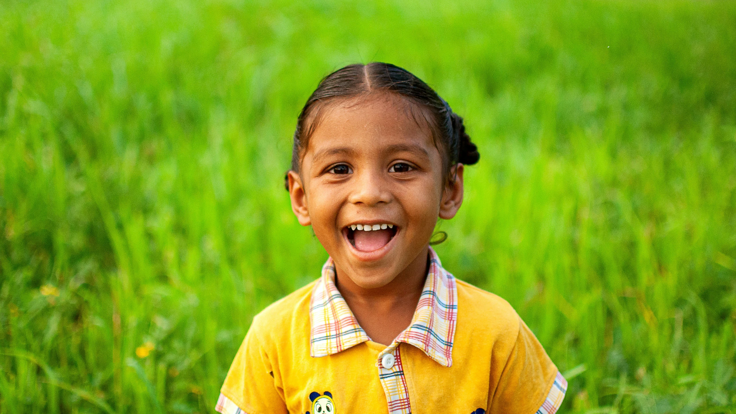 a small girl smiling while standing in a grassy field