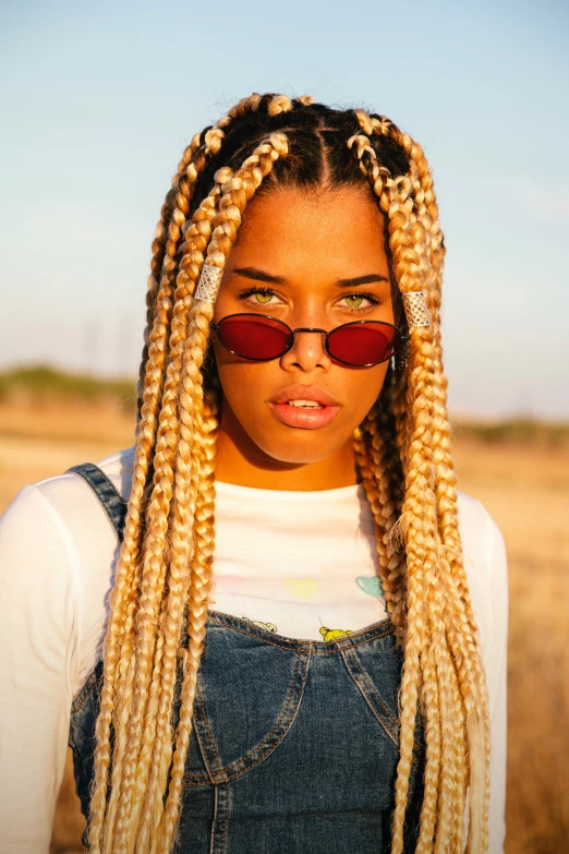 a woman with cornrows and red sunglasses stands in a desert landscape