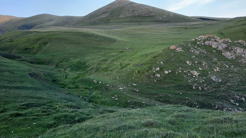 a hillside has a grassy field and three large mountains