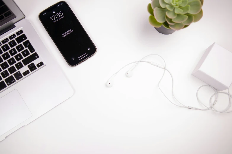 a cell phone a laptop and headphones sit on a desk