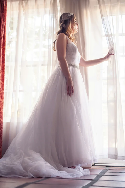 a bride stands in front of a window in a white gown