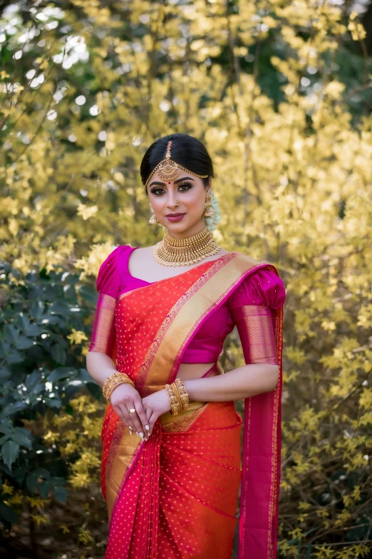 a woman wearing an indian sari and jewellery standing in a wooded area