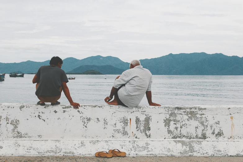 two men sitting on a concrete ledge by water