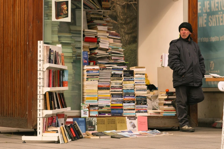 a man standing on the sidewalk near a bookstore with many books