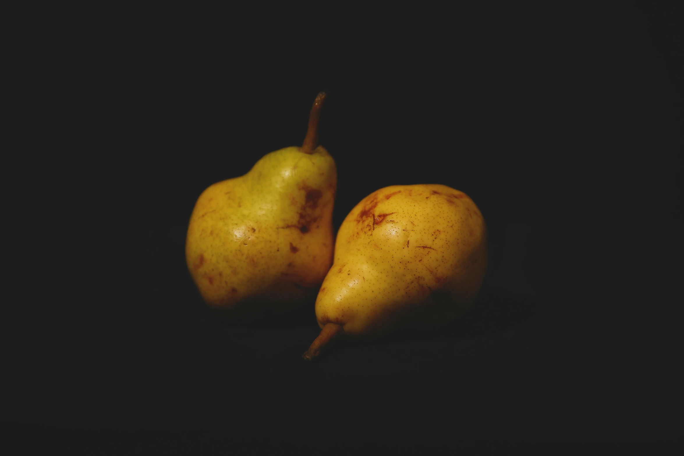 two pears sitting together on a dark surface