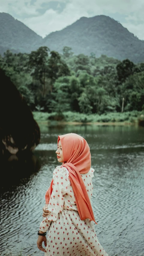 the woman is wearing a headscarf and standing in front of the lake