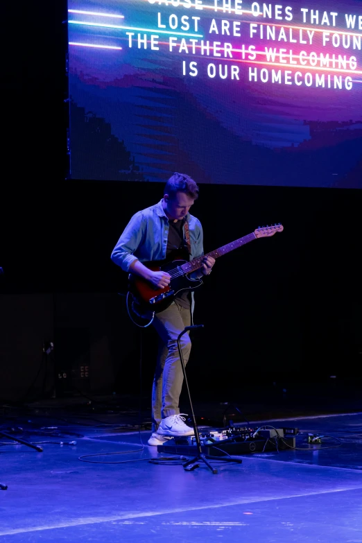 the guy is playing guitar while standing in front of the screen