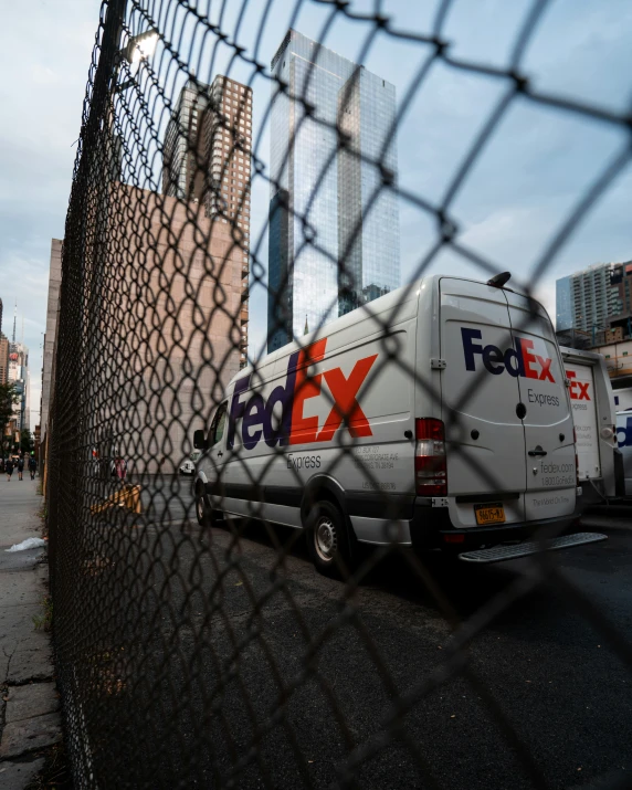 fed ex delivery truck parked on the side of the road behind the fence