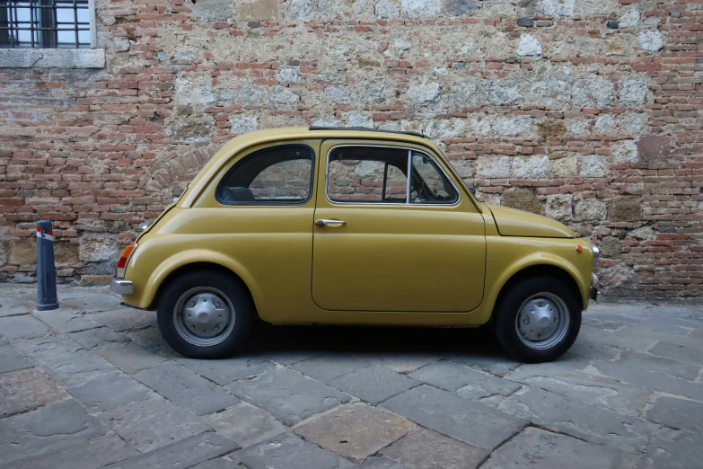 an old yellow car parked next to a red brick building