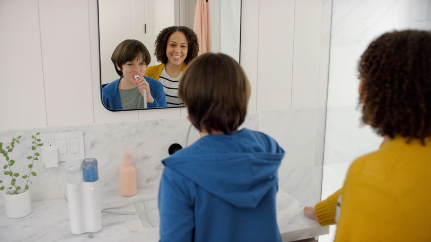 a woman brushing her teeth standing in front of a bathroom mirror