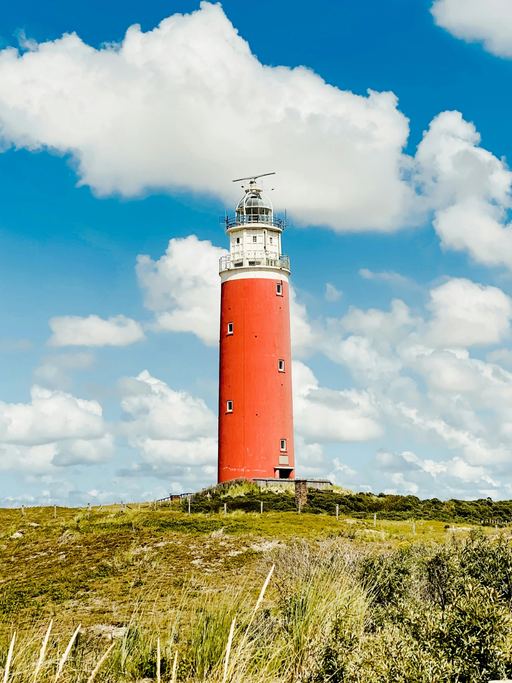 a red and white lighthouse sitting on top of a lush green hillside