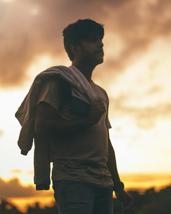 a man stands under a stormy sky as the sun goes down