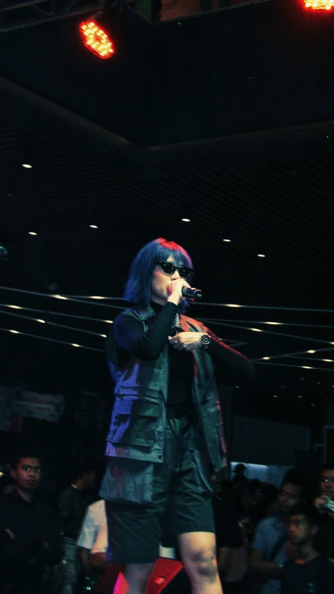 a man with an odd haircut holding a microphone in front of a crowd