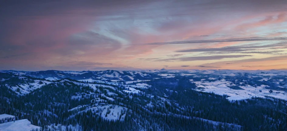 a snowy mountain range with trees and a red sky