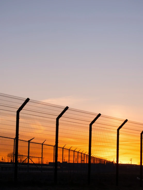 fence made up of four wire lines as the sun sets