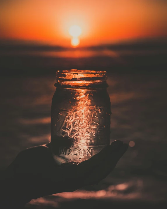 the sun is setting behind a person holding a jar