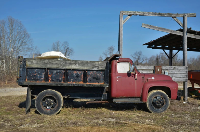 an old rusted red truck parked next to a covered structure