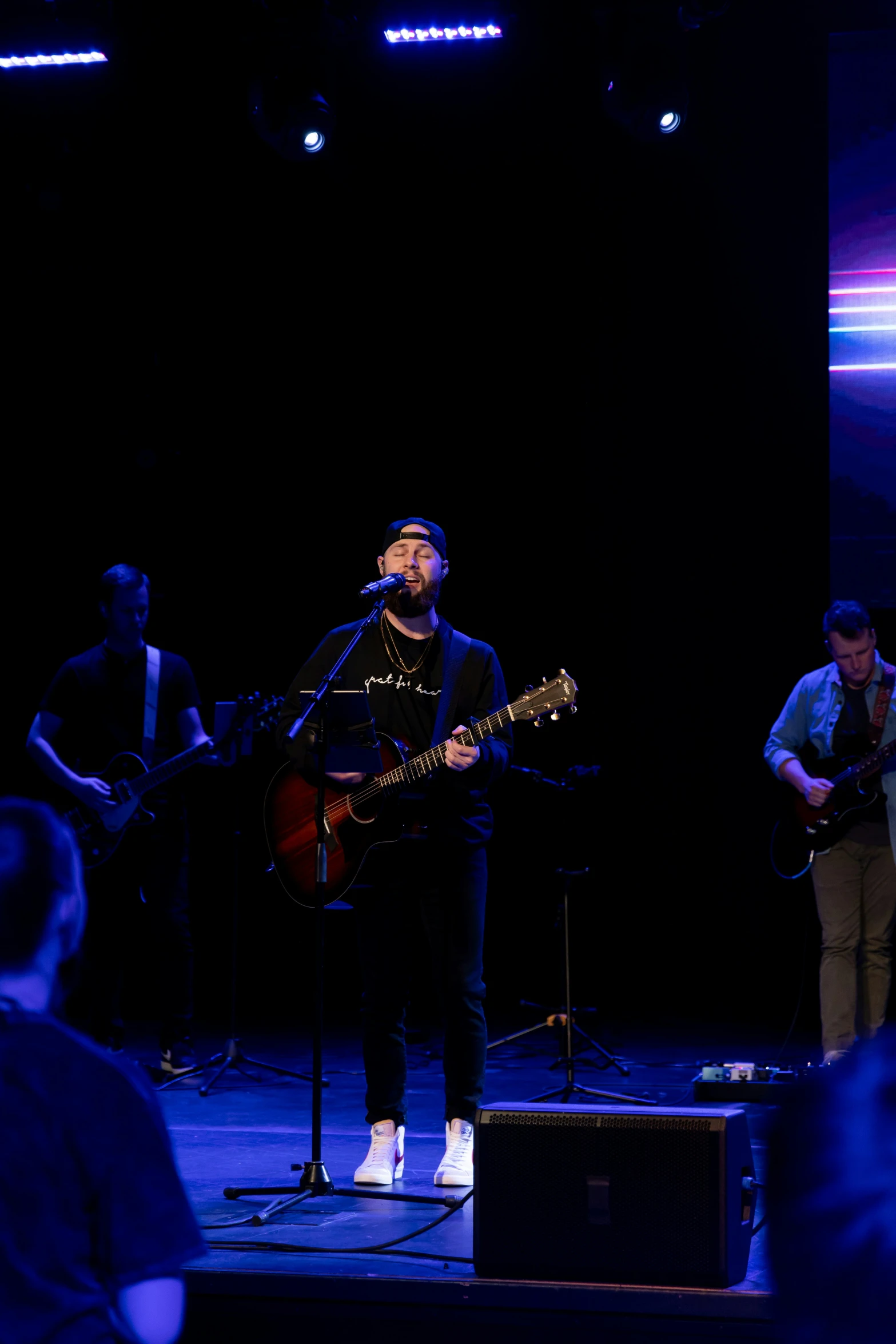 three men playing instruments on a stage with a man singing on the microphone