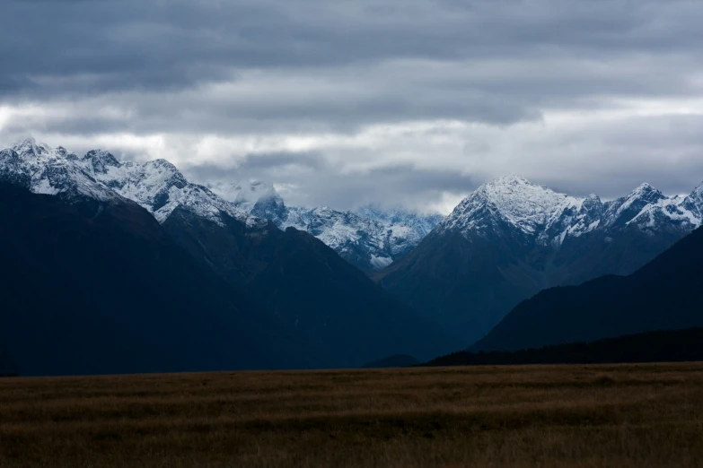 a couple of mountains covered in snow near an open field