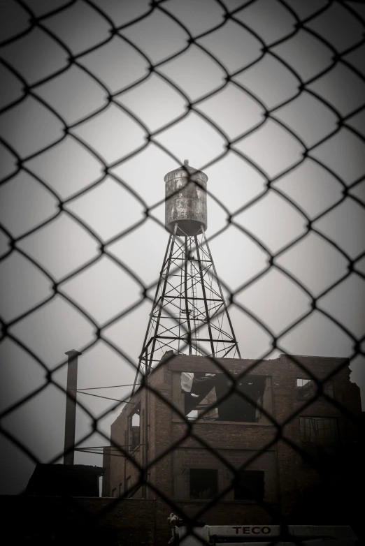 the tower that holds the watertower is viewed through a fence
