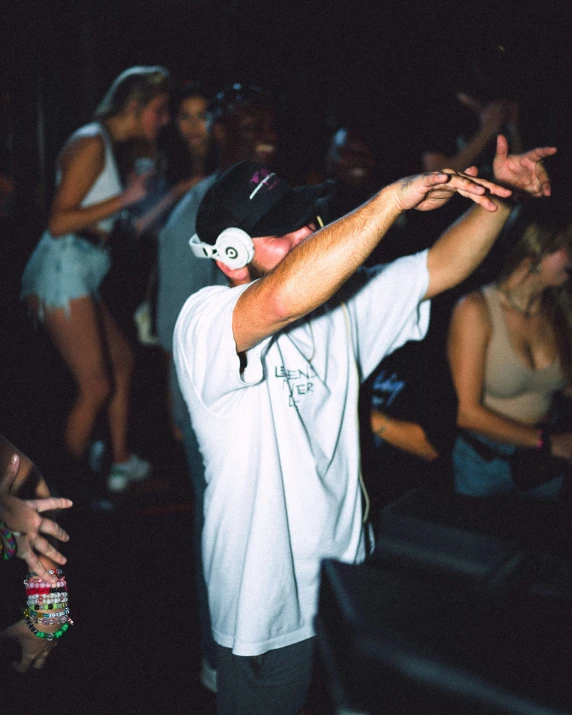 a person with a white shirt holds a drink while surrounded by people