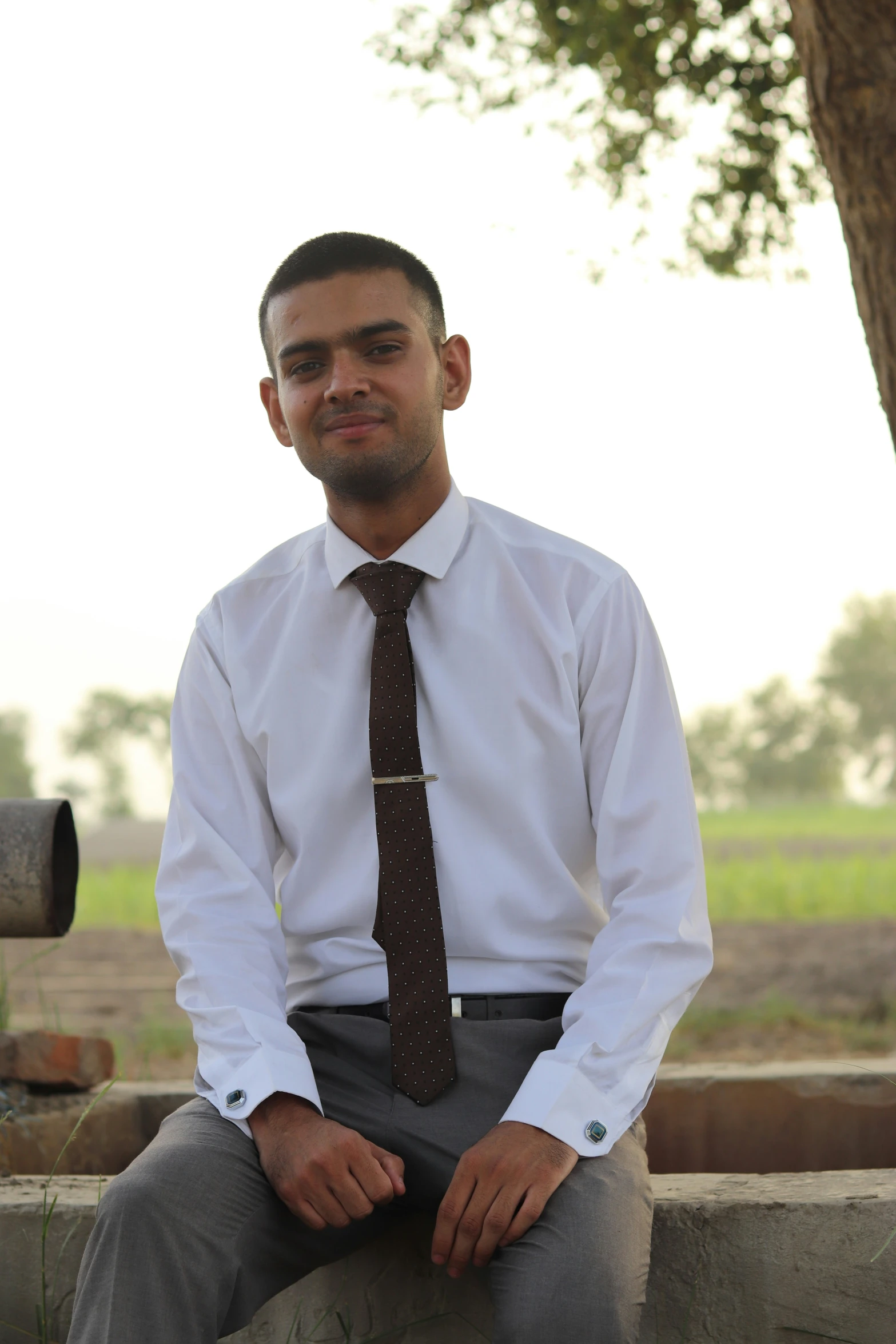 a man in tie sitting by tree in outdoors